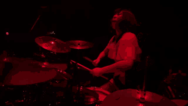 a woman is playing drums in a dark room with a red light behind her