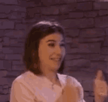 a woman is smiling and giving a thumbs up sign in front of a brick wall .