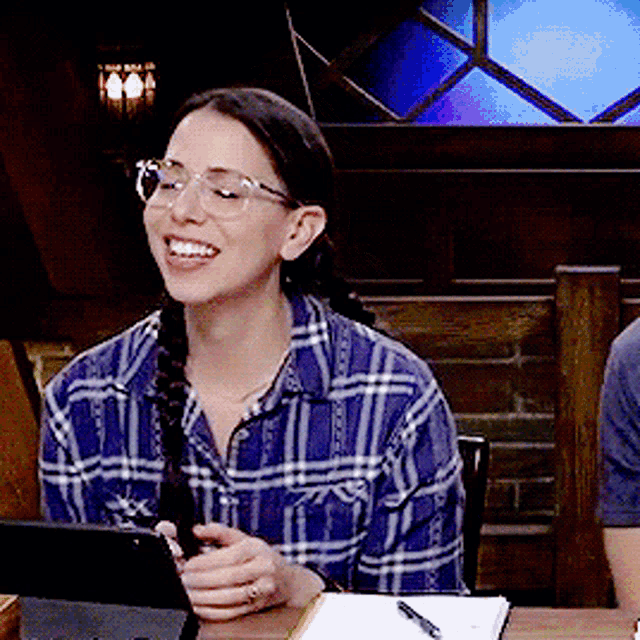 a woman wearing glasses and a plaid shirt smiles while looking at a tablet