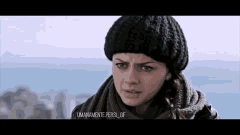 a woman in a black hat and scarf is looking at the camera .