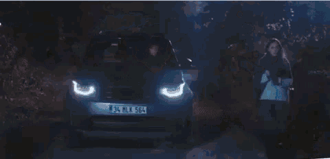 a woman is sitting in a car at night and looking at her phone .