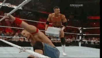 a man in a wrestling ring is holding a briefcase while another man is laying on the ground