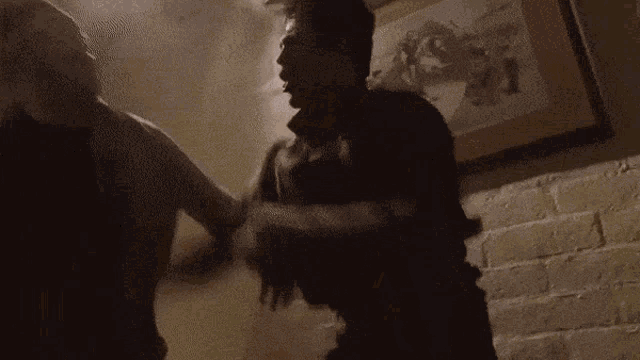 two men are fighting in a dark room with a picture in the background