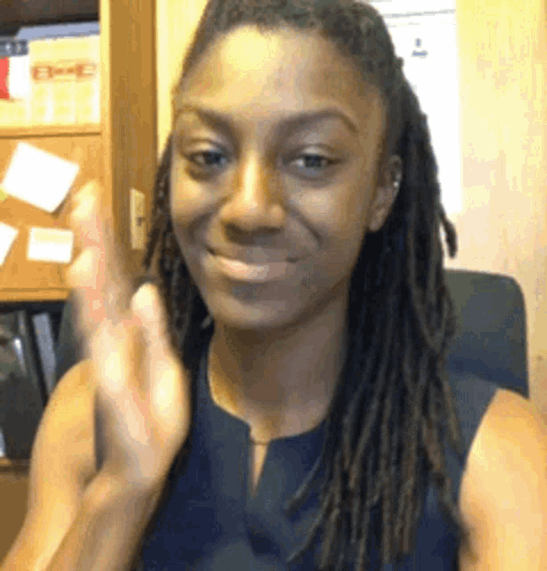 a woman with dreadlocks is smiling and clapping her hands while wearing a blue shirt .