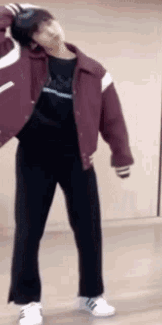 a man in a maroon jacket and black pants is standing in a room .