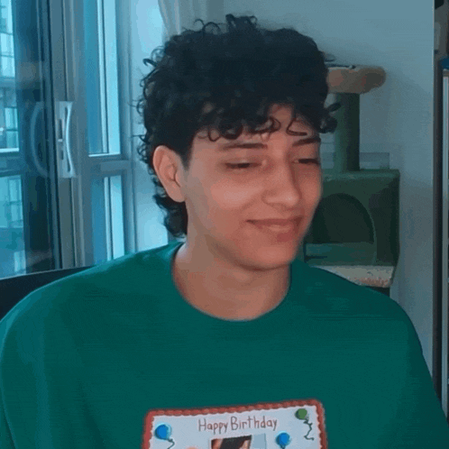 a young man with curly hair is wearing a green shirt and holding a happy birthday card .