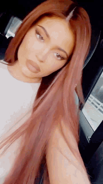 a woman with long red hair is taking a selfie in a car