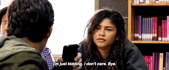 a woman is talking to a man in a library while holding a cell phone and looking at it .