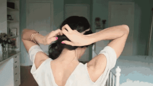a woman is putting her hair in a bun while sitting on a bed .
