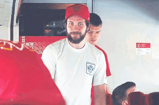 a man with a beard is wearing a red hat and a white shirt