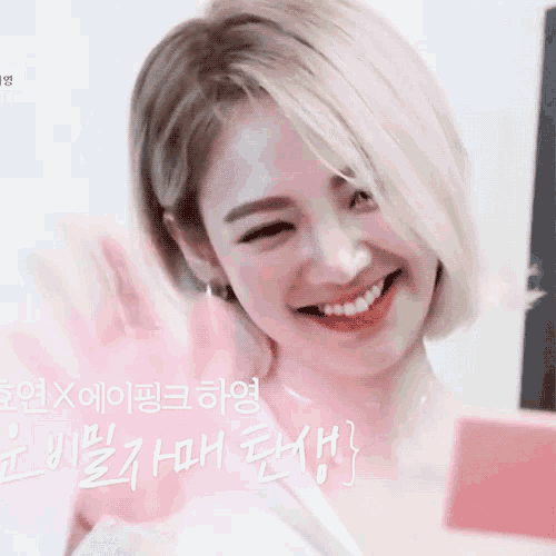 a woman with blonde hair is smiling in front of a pink background with korean writing on it