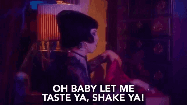 a woman in a black dress is holding a pink object and says `` oh baby let me taste ya shake ya ! ''