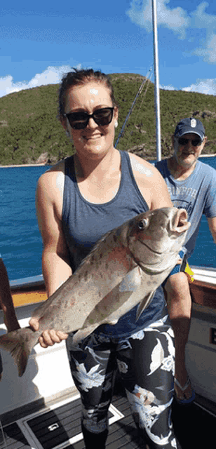 a woman holding a large fish on a boat with a man in a palm for shirt