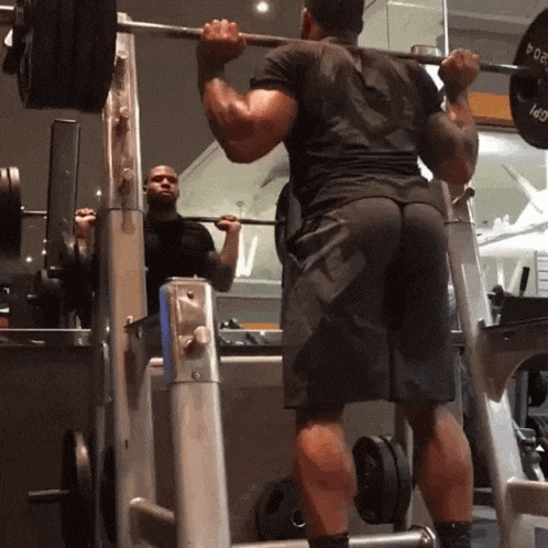 a man squatting with a barbell on his shoulders in front of a mirror that has the letter w on it