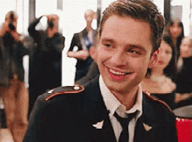 a man in a suit and tie is smiling while standing in front of a crowd of people .