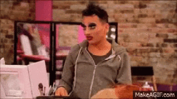 a man with makeup on his face is sitting in front of a brick wall in a room .