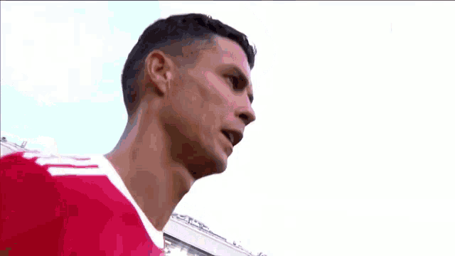 a man in a red shirt is standing in front of a stadium and looking at the camera .