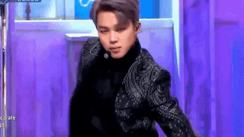 a man in a suit is dancing on a stage in front of a purple background .