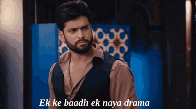 a man with a beard is standing in front of a sign that says " ek ke baadah ek naya drama "