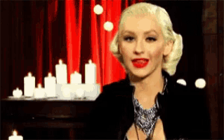 a woman stands in front of a red curtain with candles in the background