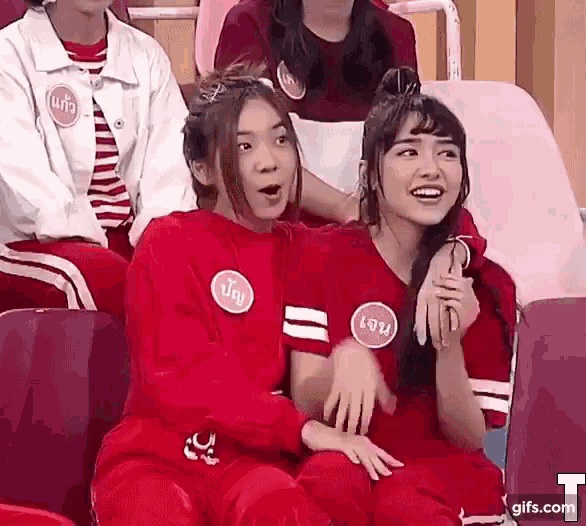 two girls in red shirts are sitting next to each other in a stadium and laughing .