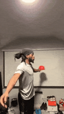 a man in a bandana is throwing a red hat in a room with a projector screen .
