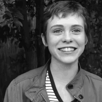 a black and white photo of a smiling young woman wearing a jacket and striped shirt .