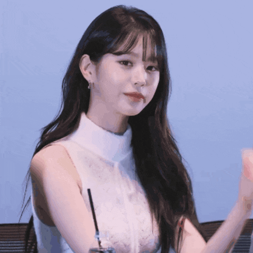 a woman in a white tank top holds a straw in her hand