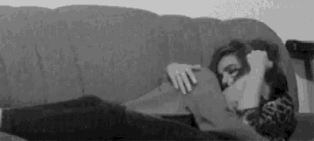 a black and white photo of a woman laying on a couch with a blanket .