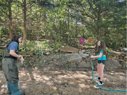 a woman and a girl are playing with a hose