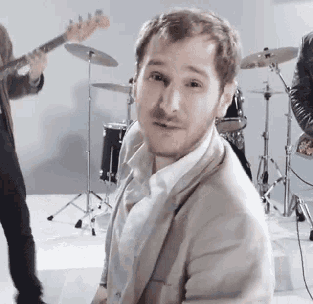 a man in a tan suit is standing in front of a drum set