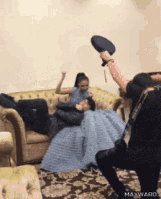 a woman in a blue dress is laying on a couch while a man throws a hat at her