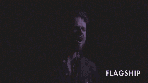 a man with a beard is standing in the dark with the word flagship below him