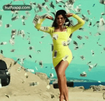 a woman in a yellow dress is standing under a pile of money .