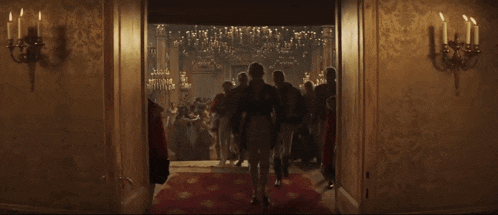 a man in a black coat with a gold star on his chest walks down a hallway