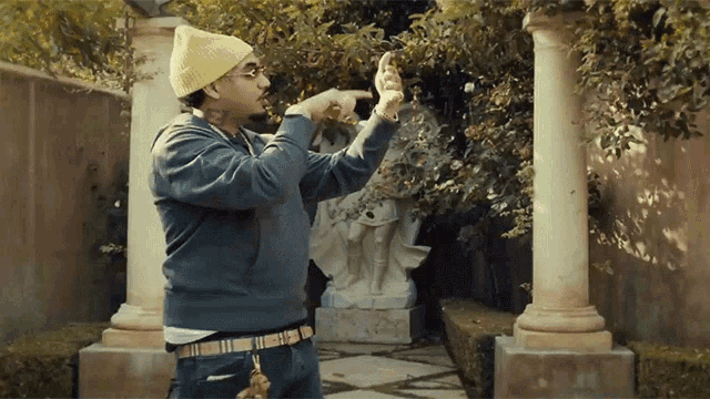 a man wearing a yellow beanie and glasses is pointing at a tree