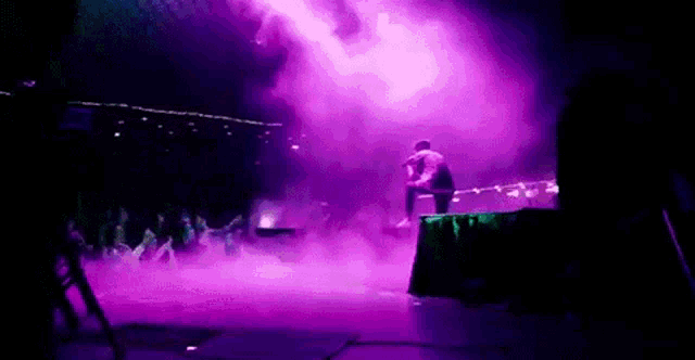 a man is kneeling on a stage with purple lights behind him