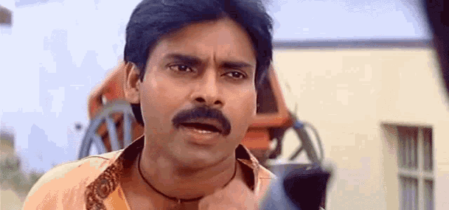 a man with a mustache is making a funny face while talking on a cell phone .