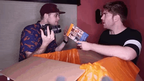 a man is holding a camera while another man holds a book .