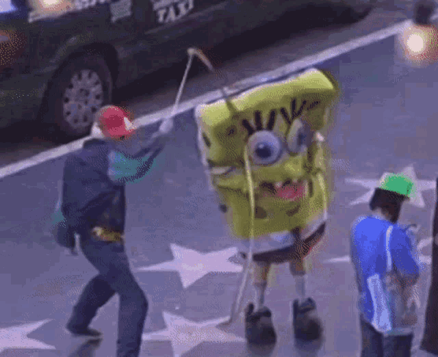 a man in a spongebob costume is walking down a street with a taxi in the background