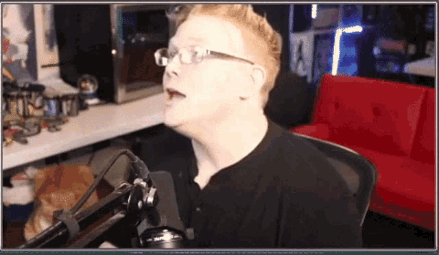 a man wearing glasses and a black shirt is speaking into a microphone