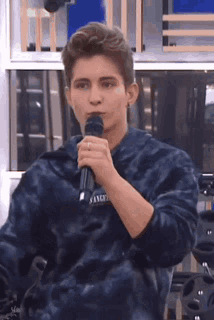a young man is holding a microphone in his mouth while wearing a tie dye sweater .