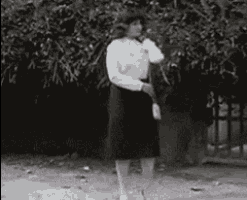 a woman in a white shirt and black skirt is standing in front of a tree in a black and white photo .