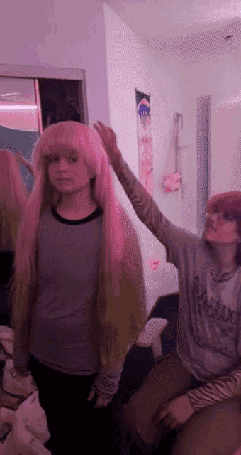a girl wearing a pink wig is being touched by another girl wearing a grey shirt that says ' army '