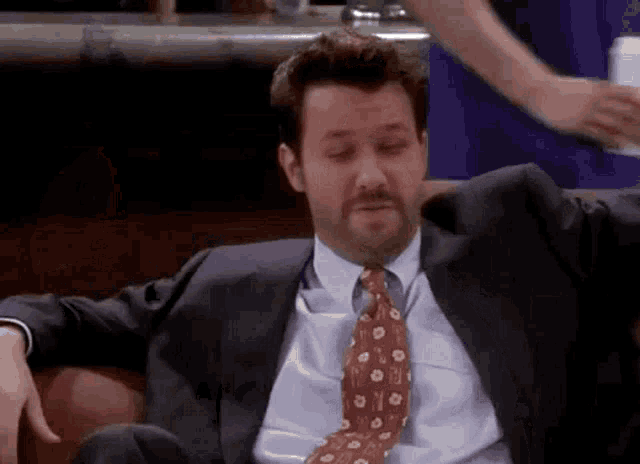 a man in a suit and tie is sitting on a couch in a bar .