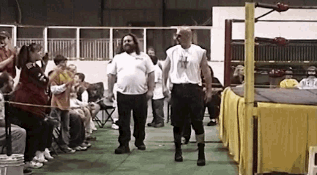 two men are walking in a wrestling ring with a crowd watching behind them