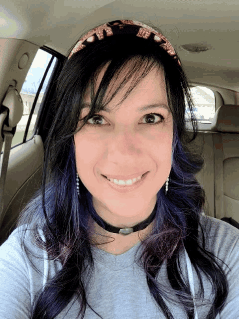 a woman with purple hair and a headband smiles for the camera