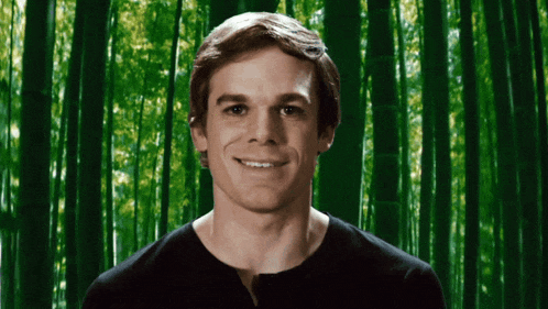 a man is smiling in front of a green background of trees