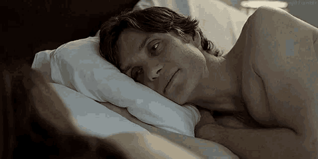 a shirtless man is laying on a bed with a pillow .