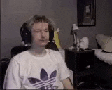 a man wearing headphones and a white adidas shirt is sitting in front of a computer screen .